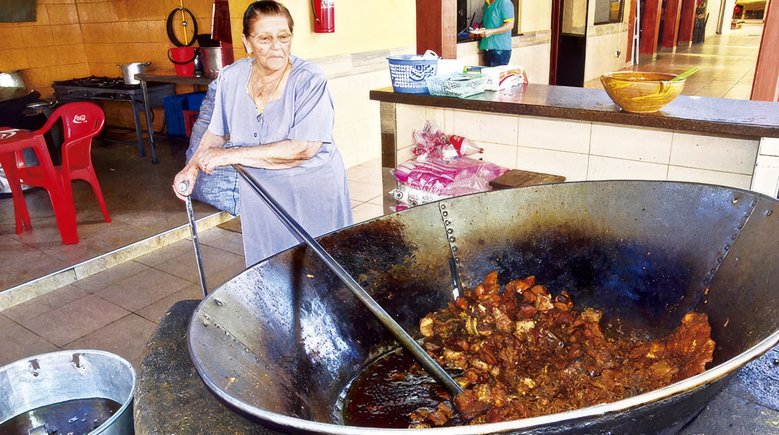 Doña Pola, sentada con su bastón junto al perol gigante de chicharrón