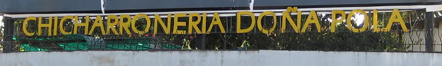 El letrero de letras amarillas CHICHARRONERIA DOÑA POLA sobre el muro de la casa