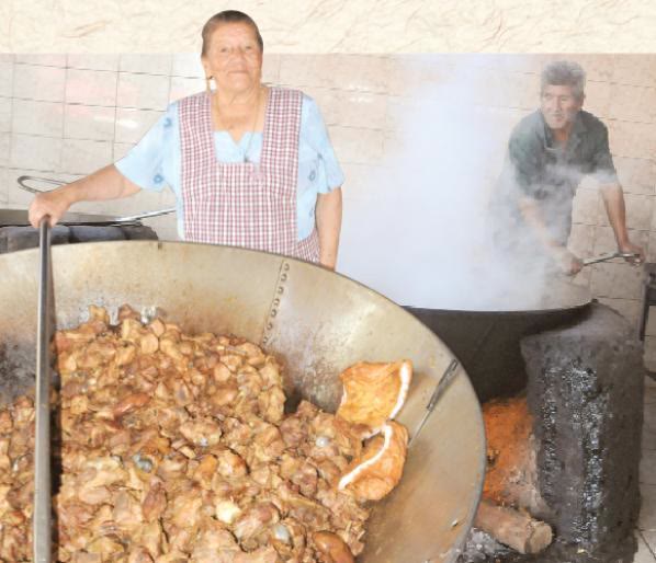 Cocinera de delantal junto a un perol colmado de chicharrón, con el vapor de un segundo perol al fondo