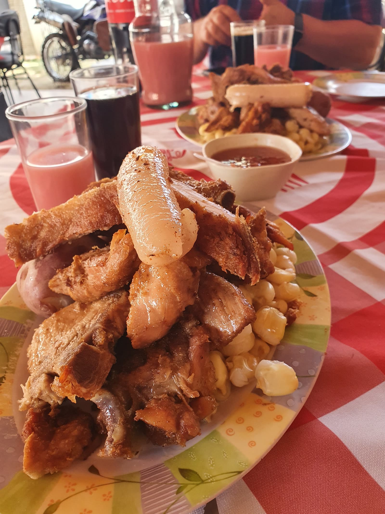 Plato de chicharrón de Doña Pola colmado sobre mote, con llajwa y vasos de garapiña en la mesa de mantel a cuadros
